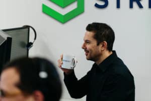 A professional man holds a "Stripe OLT" branded coffee mug in a modern office environment.